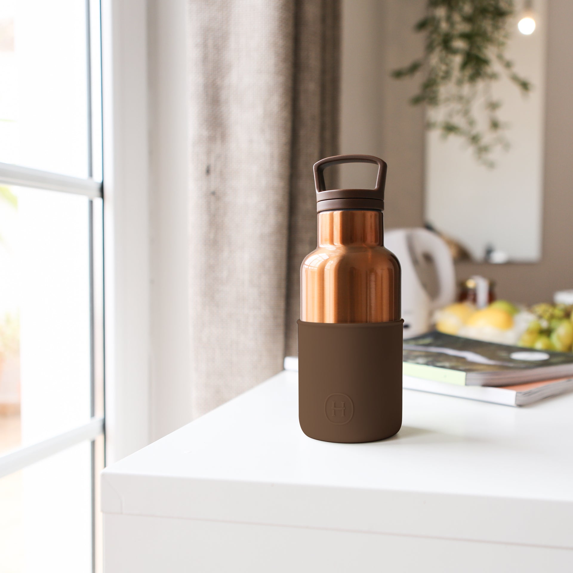 Brown and copper water bottle on a white surface with a blurred indoor background