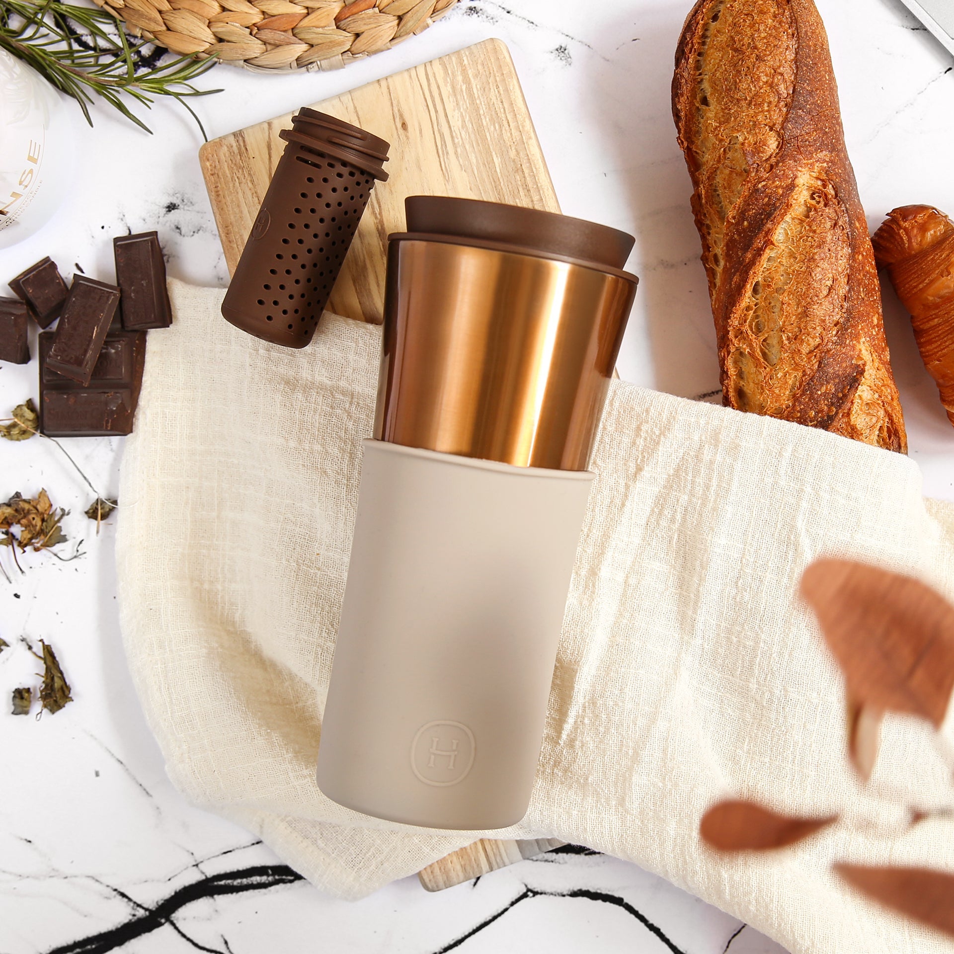 Gold and beige travel mug on a marble surface with bread and chocolate