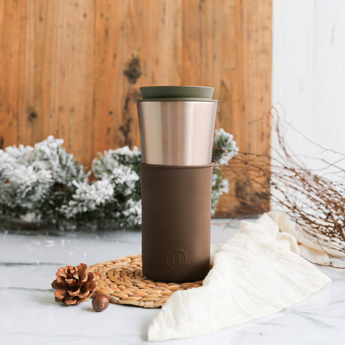 Brown and silver insulated travel mug on a wooden surface with decorative elements.