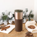 Brown and silver travel mug on a wooden surface with cookies and cinnamon sticks in the background.