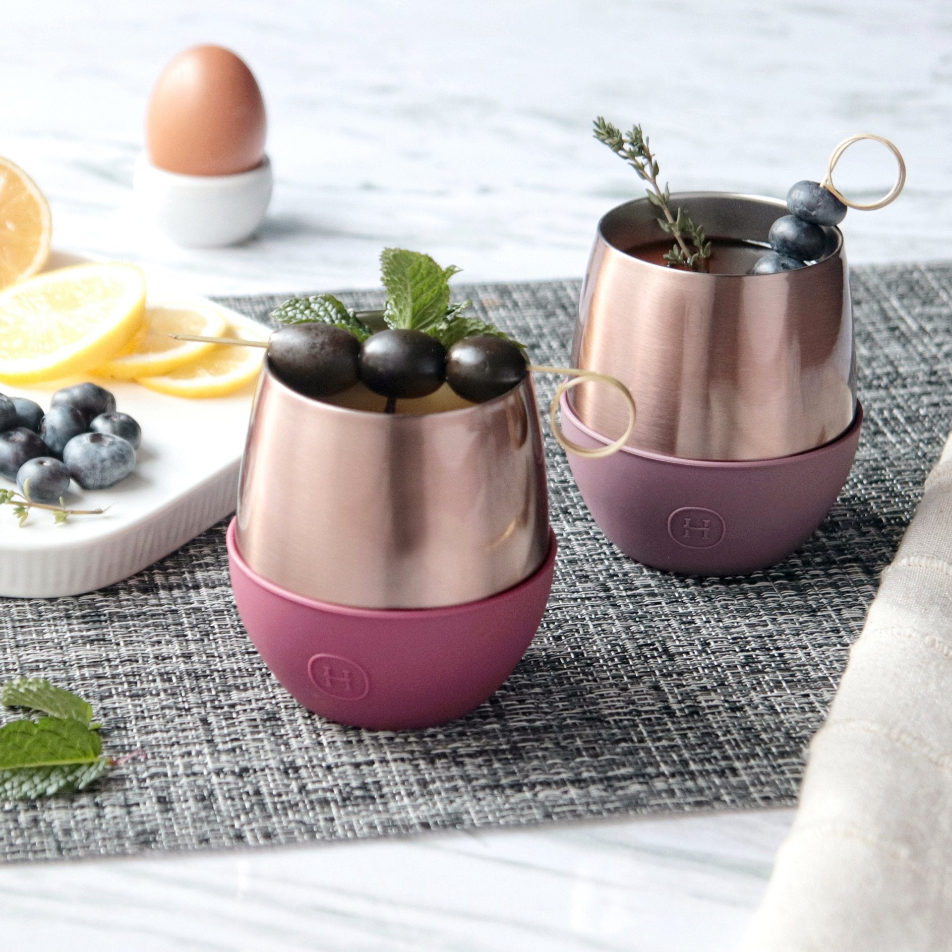 Two rose gold and pink insulated cups with fruit on a table.